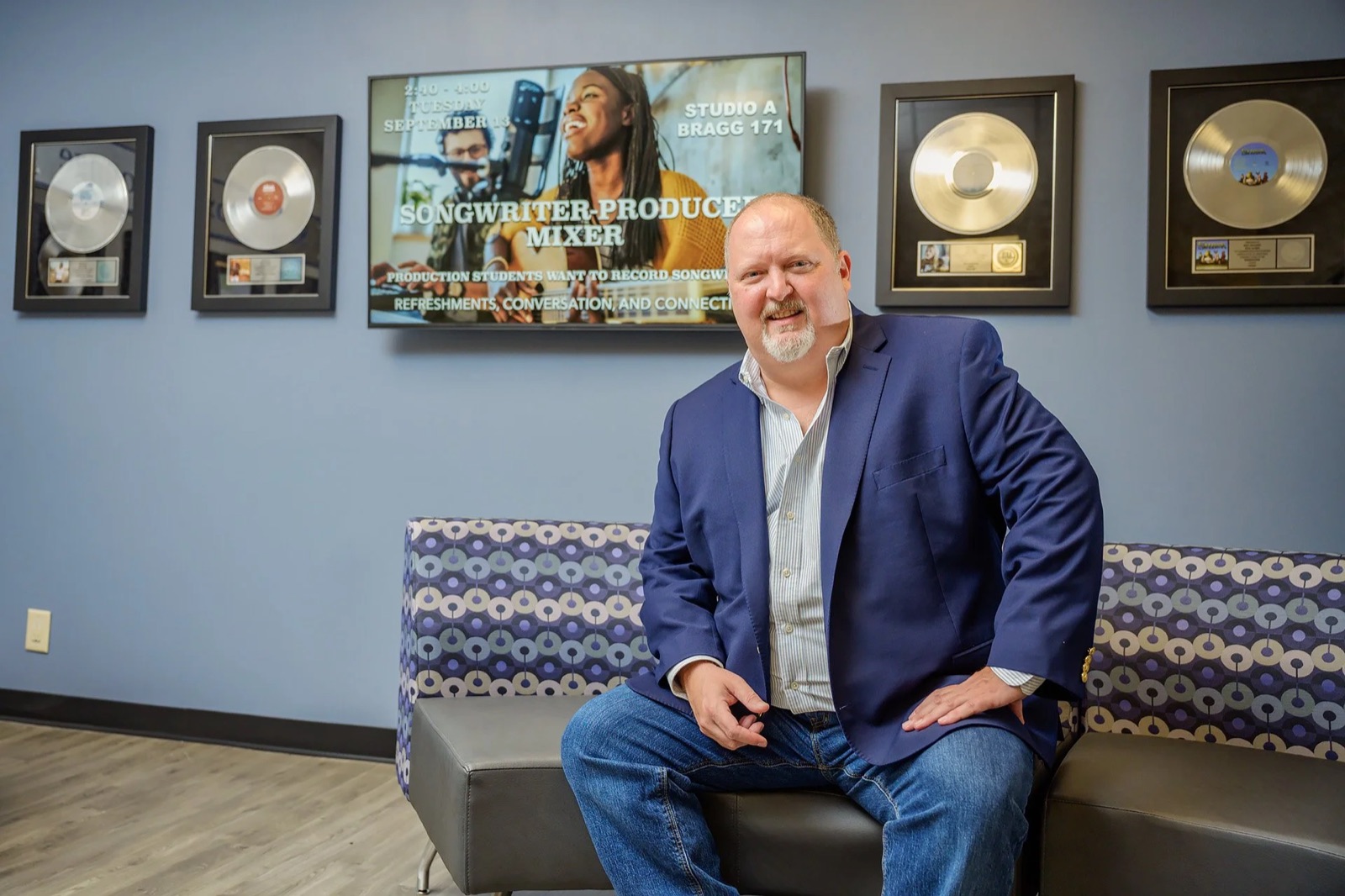 Odie Blackmon in a navy blazer, seated in front of a wall of framed platinum records.